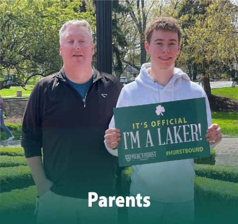 A dad posing with his son who has decided to attend ϳԹ. The son holds a poster reading "It's Official. I'm a Laker!"