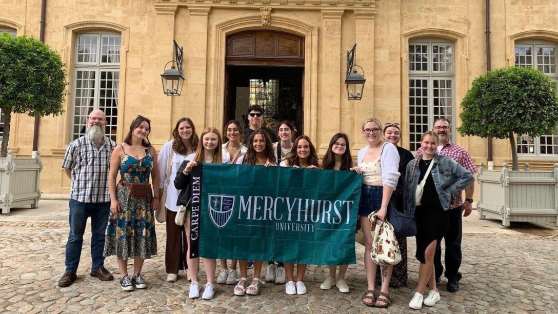 a group of students and professors pose in France with a ϳԹ flag